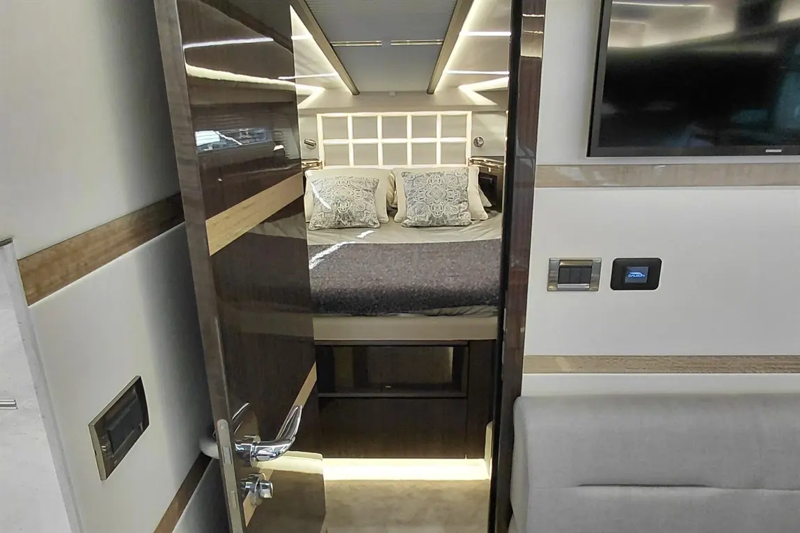Interior of a luxury yacht cabin with a bed featuring decorative pillows, a TV on the wall, and ambient lighting.